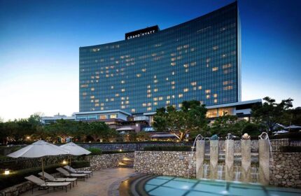 Grand Hyatt Seoul, a gay-friendly hotel. Exterior view of the hotel at dusk, showing the pool area with lounge chairs and fountain.