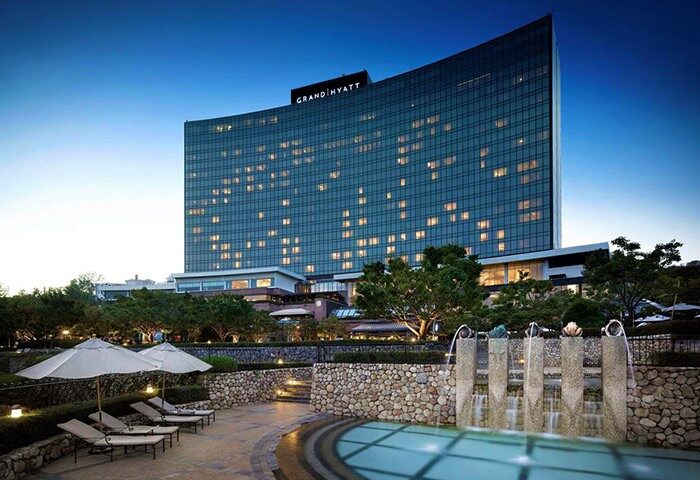 Grand Hyatt Seoul, a gay-friendly hotel. Exterior view of the hotel at dusk, showing the pool area with lounge chairs and fountain.