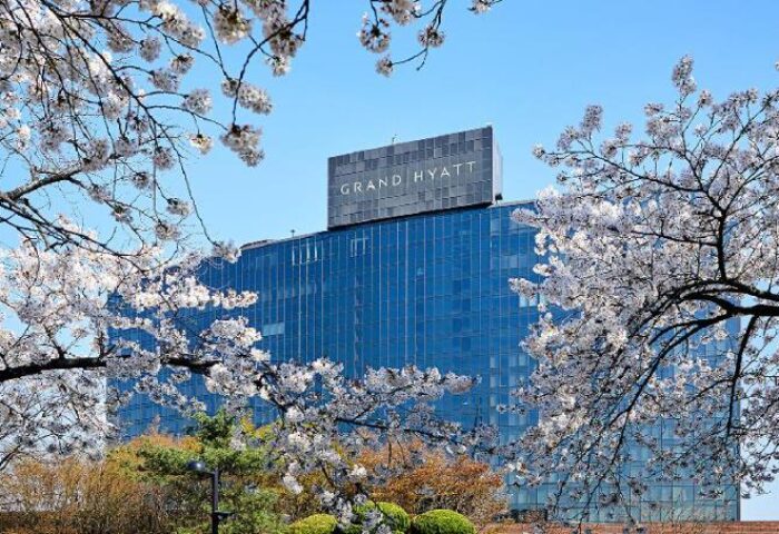 Grand Hyatt Seoul, a gay-friendly hotel, framed by cherry blossoms. Blue glass facade with the hotel's name on top. A luxury choice for gay travelers.