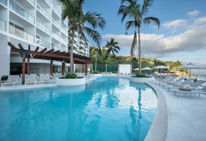 Grand Park Royal Puerto Vallarta All-Inclusive pool view. Gay-friendly hotel with palm trees, lounge chairs, and ocean view. Ideal for gay travel.