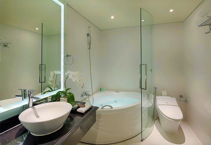 Grand Silverland Hotel bathroom. Modern design with a round tub, glass partition, sleek sink, and toilet. Gay-friendly hotel amenities.