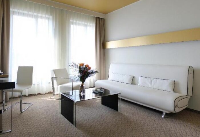 Grandior Hotel Prague room. Modern interior with white sofa, chairs, and glass table. Gay-friendly hotel for gay men's travel advice.