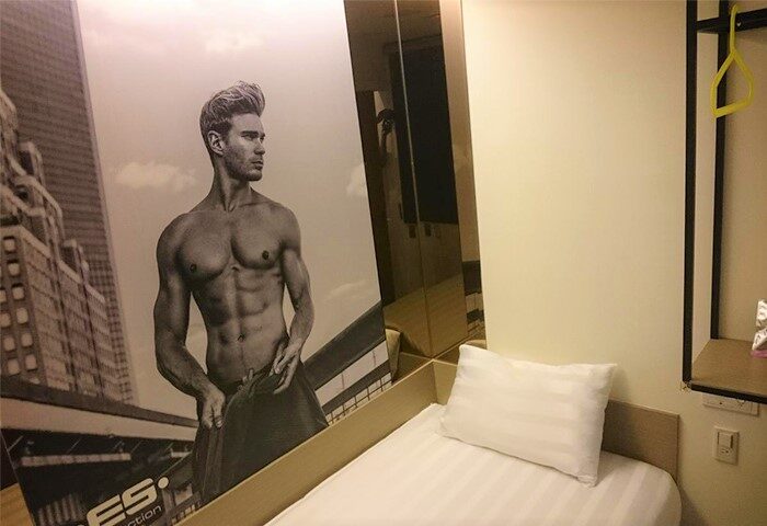 Gs Gay Hotel room. Gay-friendly hotel with a toned man mural on the wall. Single bed with white sheets and pillow. Modern, clean design.