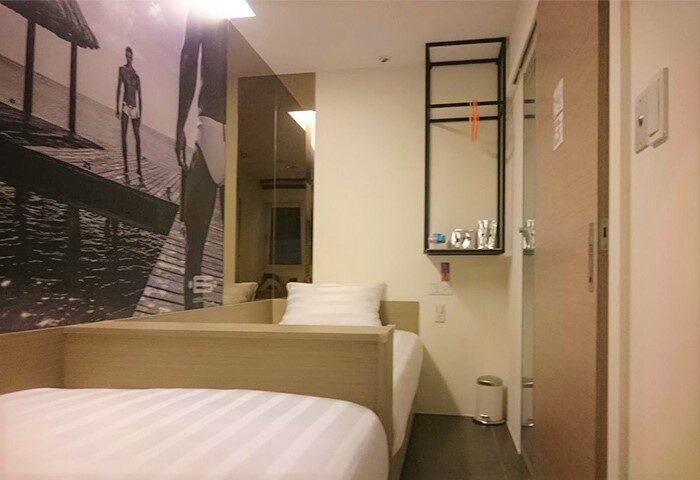 Gs Gay Hotel room. Gay-friendly hotel with modern design. Single bed with striped sheets, beach themed wall art, and a minimalist shelf.
