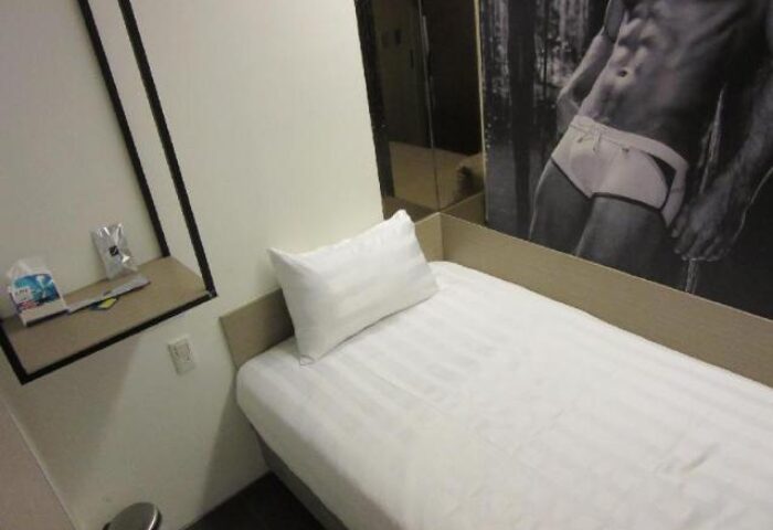 Gs Gay Hotel room interior. Single bed with white sheets. Wall art of a muscular man. Gay-friendly hotel for gay men travel advice.