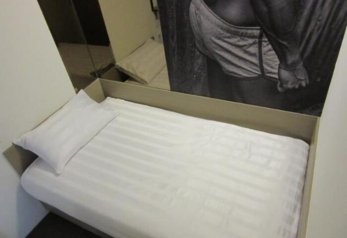 Gs Gay Hotel room. Single bed with white linens and pillow. Black and white photo of a man's torso on the wall. Gay-friendly hotel.