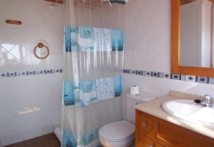 Bathroom at Guadalupe Cozy Inns, a gay-friendly hotel. Features a shower with curtain, toilet, sink, and wooden accents.