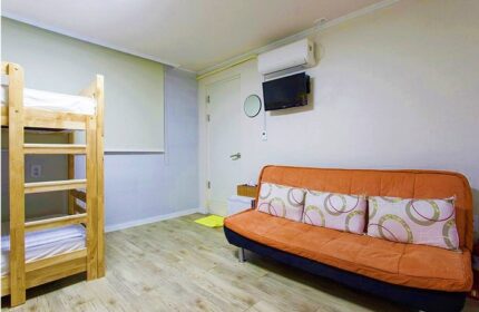 Guest House DODAMi room. Gay-friendly hotel with bunk beds, orange sofa, and TV. Ideal lodging for gay travelers.