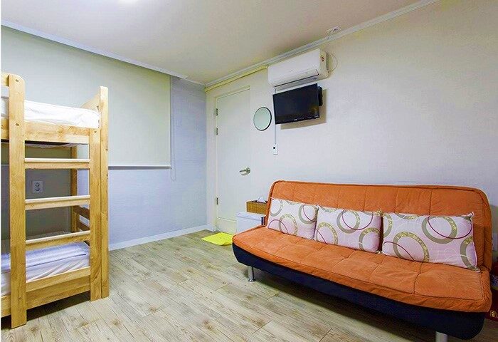 Guest House DODAMi room. Gay-friendly hotel with bunk beds, orange sofa, and TV. Ideal lodging for gay travelers.