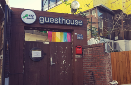 Entrance to Guest House DODAMi, a gay-friendly hotel. The guesthouse has a wooden gate and a rainbow decoration. Gay travel advice.