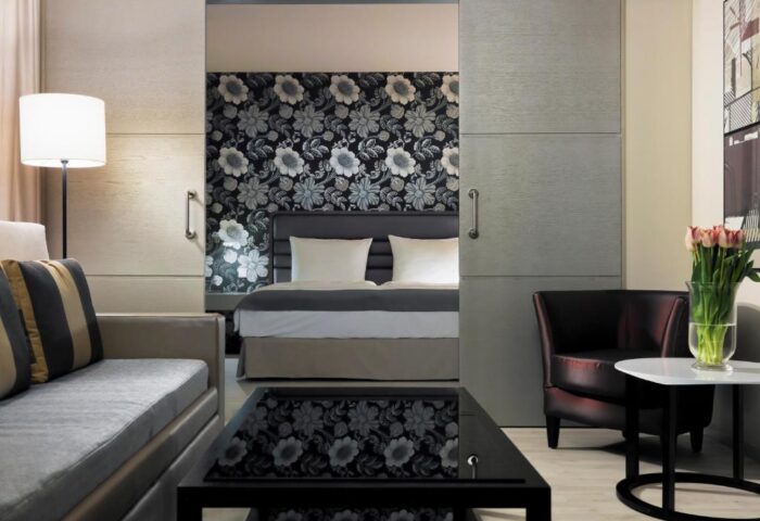 H10 Berlin Ku'damm Hotel suite. Gay-friendly hotel room with sofa, bed, floral wallpaper, and sliding doors. Modern decor.