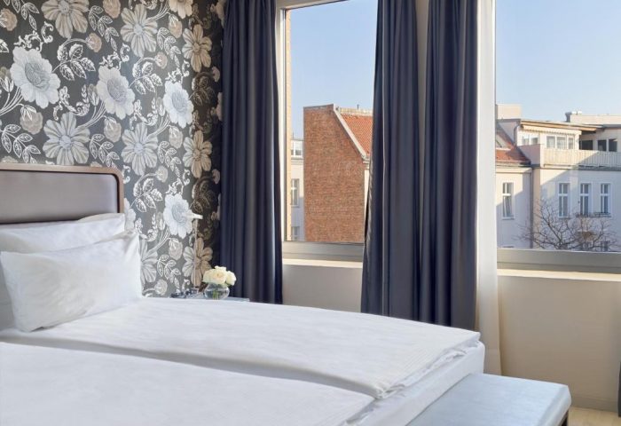 H10 Berlin Ku'damm Hotel room. Gay-friendly hotel bedroom with floral wallpaper, white linens, and window view. Kudamm gay travel lodging.