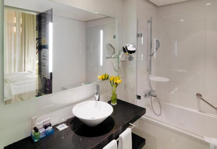 H10 Berlin Ku'damm Hotel bathroom. Modern design with sink, mirror, and bathtub. Gay-friendly hotel in Berlin.