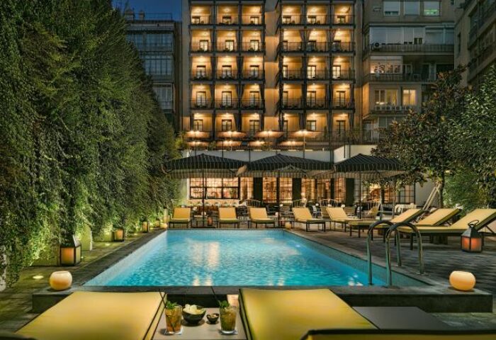 H10 Metropolitan Hotel pool at night. Gay-friendly hotel with lounge chairs, umbrellas, and drinks. A perfect gay travel destination.