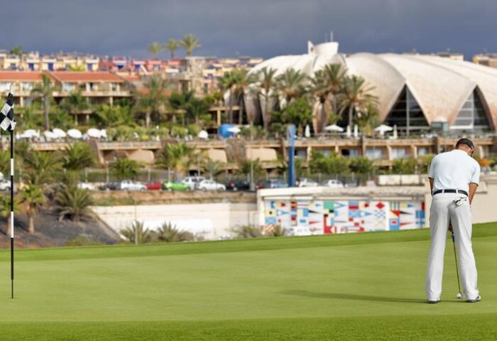 Gay-Friendly H10 Playa Meloneras Palace golf course view. Golfer putting on the green. Upscale resort in the background. Gran Canaria gay travel.