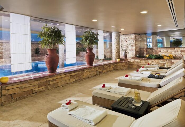 H10 Playa Meloneras Palace's gay-friendly spa. Loungers line a stone wall with plants and a pool view. Relaxing gay travel destination.