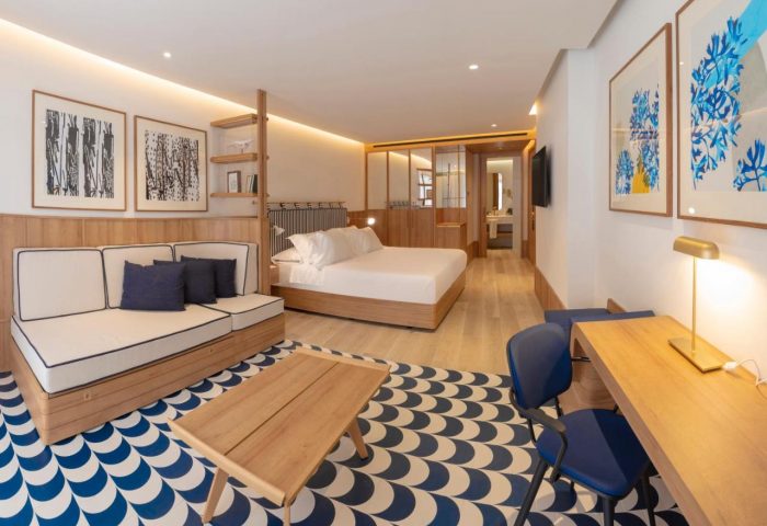 H10 Porto Poniente 4* Sup gay-friendly hotel room. Modern design with bed, sofa, desk, and blue/white patterned rug. Stylish Benidorm stay.
