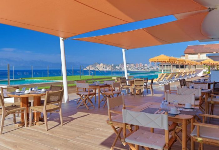 H10 Porto Poniente 4* Sup gay-friendly hotel's outdoor dining area with sea view. Tables and chairs under a sunshade near the pool.