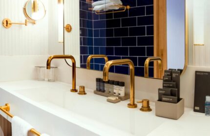 H10 Porto Poniente bathroom. Double sink with gold fixtures, toiletries, and blue tiled wall. Gay-friendly hotel detail.