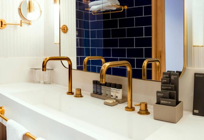 H10 Porto Poniente bathroom. Double sink with gold fixtures, toiletries, and blue tiled wall. Gay-friendly hotel detail.