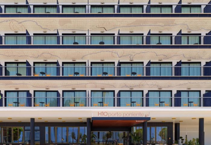 H10 Porto Poniente 4* Sup gay-friendly hotel facade. Modern design, balconies, and entrance with yellow benches. Gay travel in Benidorm.