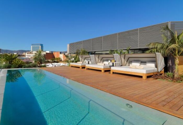 H10 The One Barcelona gay-friendly hotel rooftop pool. Loungers and palm trees offer a relaxing vibe in this Barcelona travel destination.