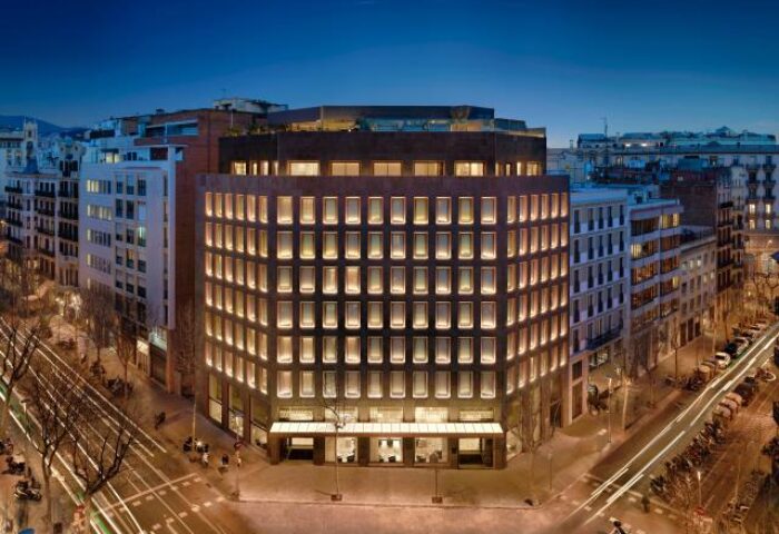 Exterior of H10 The One Barcelona, a gay-friendly hotel. Evening view of the illuminated building and city streets. Great choice for gay travel.