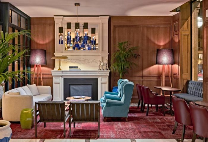 H10 Villa de la Reina Boutique Hotel lobby. Gay-friendly hotel interior with fireplace, blue chairs, and red rug. Cozy, inviting space.