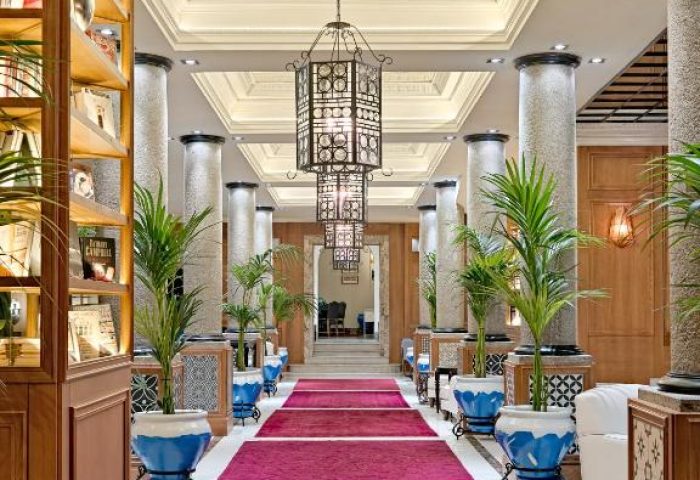 H10 Villa de la Reina Boutique Hotel lobby. Gay-friendly hotel with red carpets, plants, and columns. Upscale interior design.