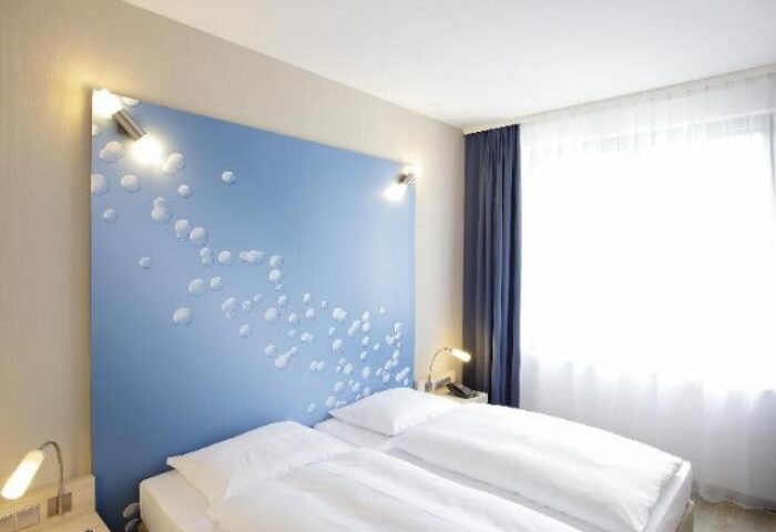 H2 Hotel Berlin-Alexanderplatz room. Double bed with white linens, blue headboard with bubble design. Gay-friendly hotel in Berlin, Germany.