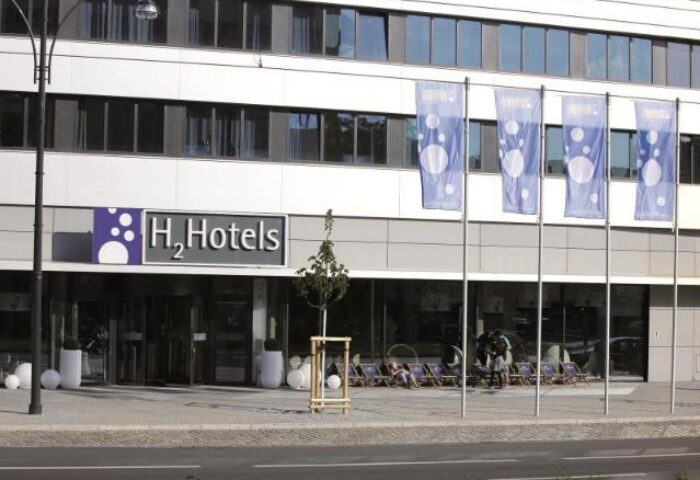 H2 Hotel Berlin Alexanderplatz exterior. Gay-friendly hotel with modern design, flags, and outdoor seating. A great choice for gay travelers in Berlin.