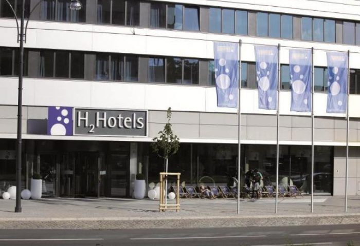 H2 Hotel Berlin Alexanderplatz exterior. Gay-friendly hotel with modern design, flags, and outdoor seating. A great choice for gay travelers in Berlin.