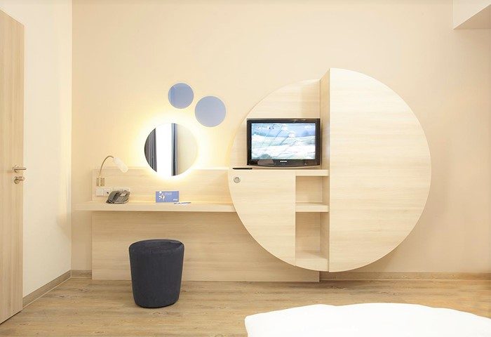 H2 Hotel Berlin-Alexanderplatz room. Modern design with desk, TV, round mirror, and stool. Gay-friendly hotel for your Berlin visit.