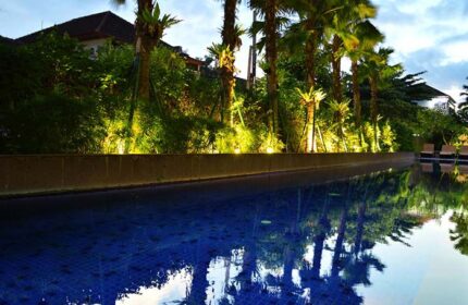 HARRIS Hotel Seminyak pool view. Gay-friendly hotel with palm trees reflecting in the water. A relaxing spot for gay travelers in Seminyak.