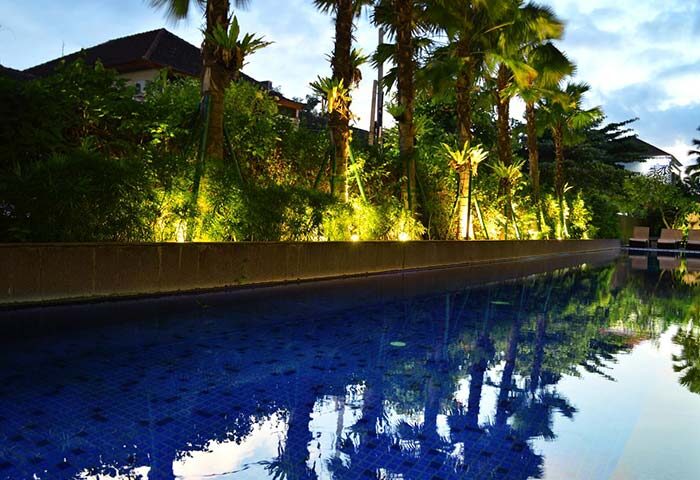 HARRIS Hotel Seminyak pool view. Gay-friendly hotel with palm trees reflecting in the water. A relaxing spot for gay travelers in Seminyak.