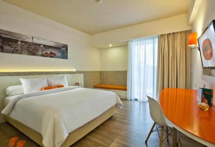 HARRIS Hotel Seminyak room. Gay-friendly hotel bedroom with white linens, orange accents, desk, and TV. Modern design for gay travelers.