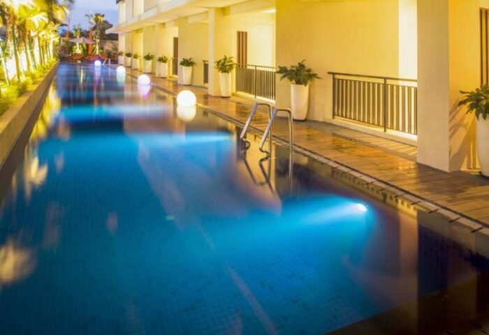 HARRIS Hotel Seminyak pool at dusk. Gay-friendly hotel with modern design, blue-lit pool, and poolside plants. Ideal for gay travel in Seminyak.