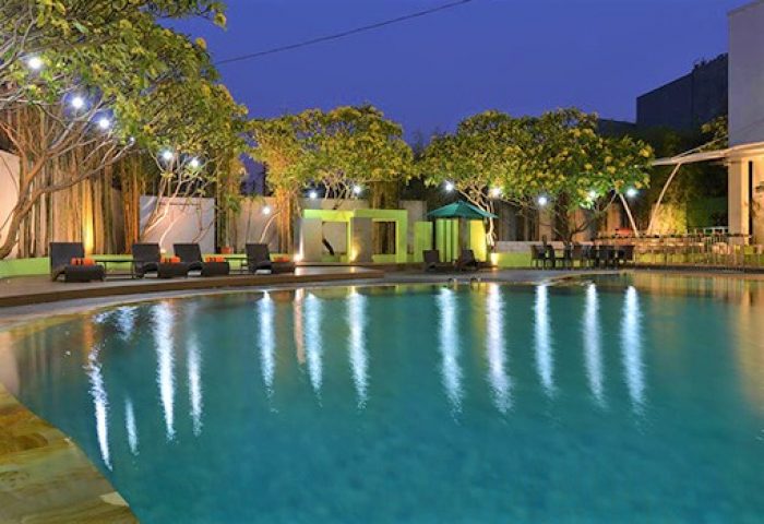 Pool at HARRIS Hotel Tebet, a gay-friendly hotel. Evening view with lounge chairs, trees, and reflections in the water. Jakarta, Indonesia.