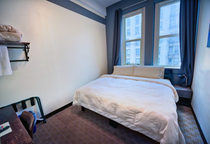 HI Chicago Hostel room. Gay-friendly hotel with a bed, two windows, and blue curtains. Budget travel lodging for gay men in Chicago.