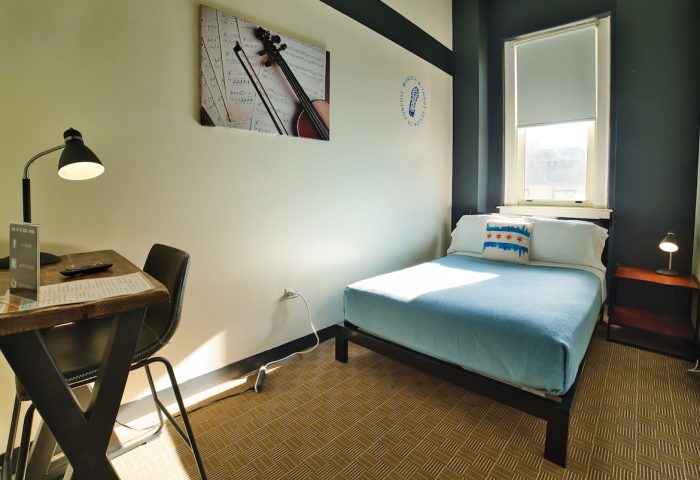 HI Chicago Hostel gay-friendly hotel room. Single bed with Chicago skyline pillow, desk, and violin art. Budget travel for gay men.