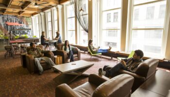 HI Chicago Hostel's gay-friendly hotel lounge. People relax in leather chairs, by large windows, and at tables. A social, inviting space.