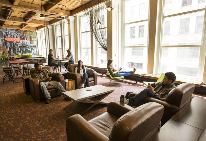 HI Chicago Hostel's gay-friendly hotel lounge. People relax in leather chairs, by large windows, and at tables. A social, inviting space.