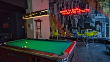 HI Chicago Hostel's game room with a pool table, bar stools, and a neon sign that reads Forget the maps... follow your instincts. Gay-friendly hotel.