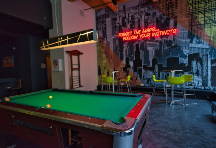 HI Chicago Hostel's game room with a pool table, bar stools, and a neon sign that reads Forget the maps... follow your instincts. Gay-friendly hotel.