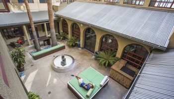 HI Los Angeles Santa Monica Hostel courtyard view. Gay-friendly hotel with fountain, plants, lounge area, and person relaxing on a daybed.