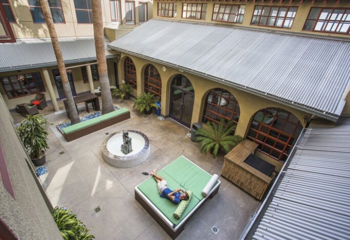 HI Los Angeles Santa Monica Hostel courtyard view. Gay-friendly hotel with fountain, plants, lounge area, and person relaxing on a daybed.