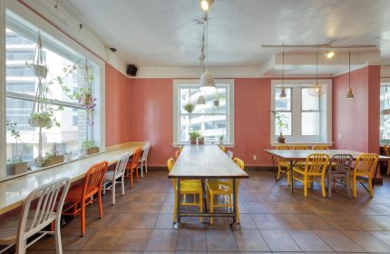 HI San Francisco Downtown Hostel's dining area. Gay-friendly hotel with tables, chairs, windows, and plants. A welcoming space for travelers.