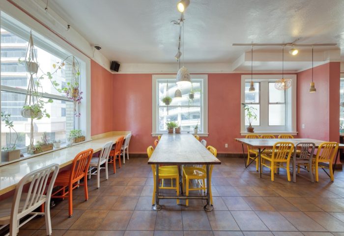 HI San Francisco Downtown Hostel's dining area. Gay-friendly hotel with tables, chairs, windows, and plants. A welcoming space for travelers.