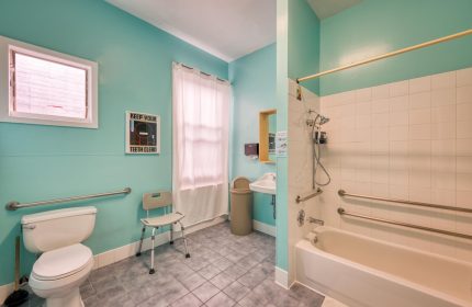 Bathroom at HI San Francisco Downtown Hostel, a gay-friendly hotel. Accessible features include grab bars, shower seat, and toilet.