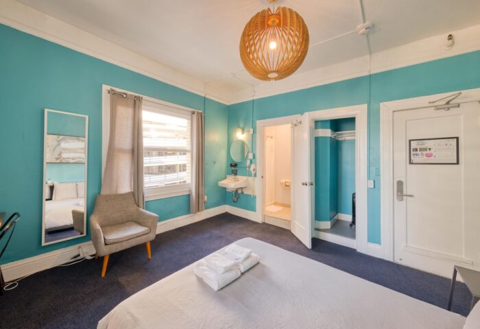 HI San Francisco Downtown Hostel room. Gay-friendly hotel room featuring a bed, chair, and ensuite bathroom. Turquoise walls.